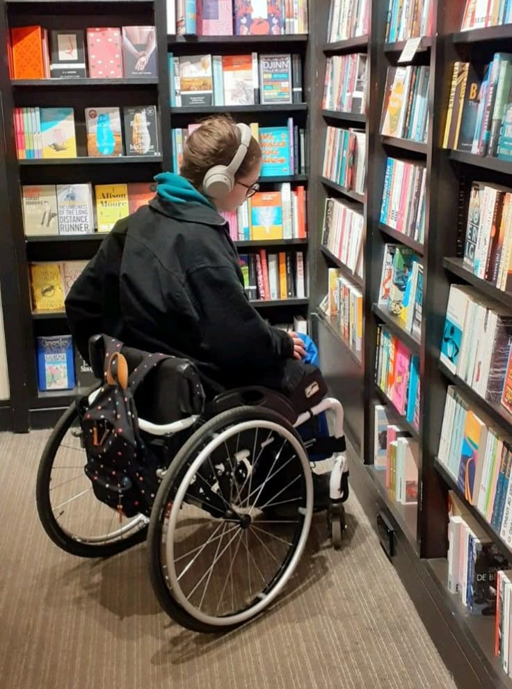 Person in wheelchair in a bookstore looking for books. Person in wheelchair in a bookstore looking for books.