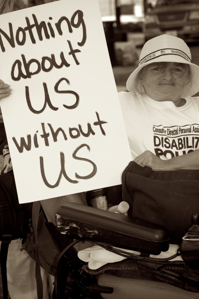 Photo of woman in wheelchair holding sign saying nothing about us without us
